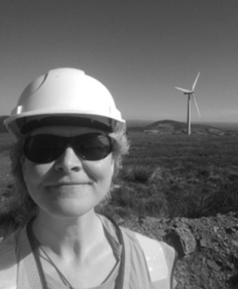 A woman in front of a wind turbine wearing a hard hat